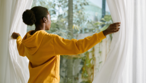 Pessoa abrindo as cortinas pela manhã para receber luz natural, um dos melhores hábitos para acordar com energia.